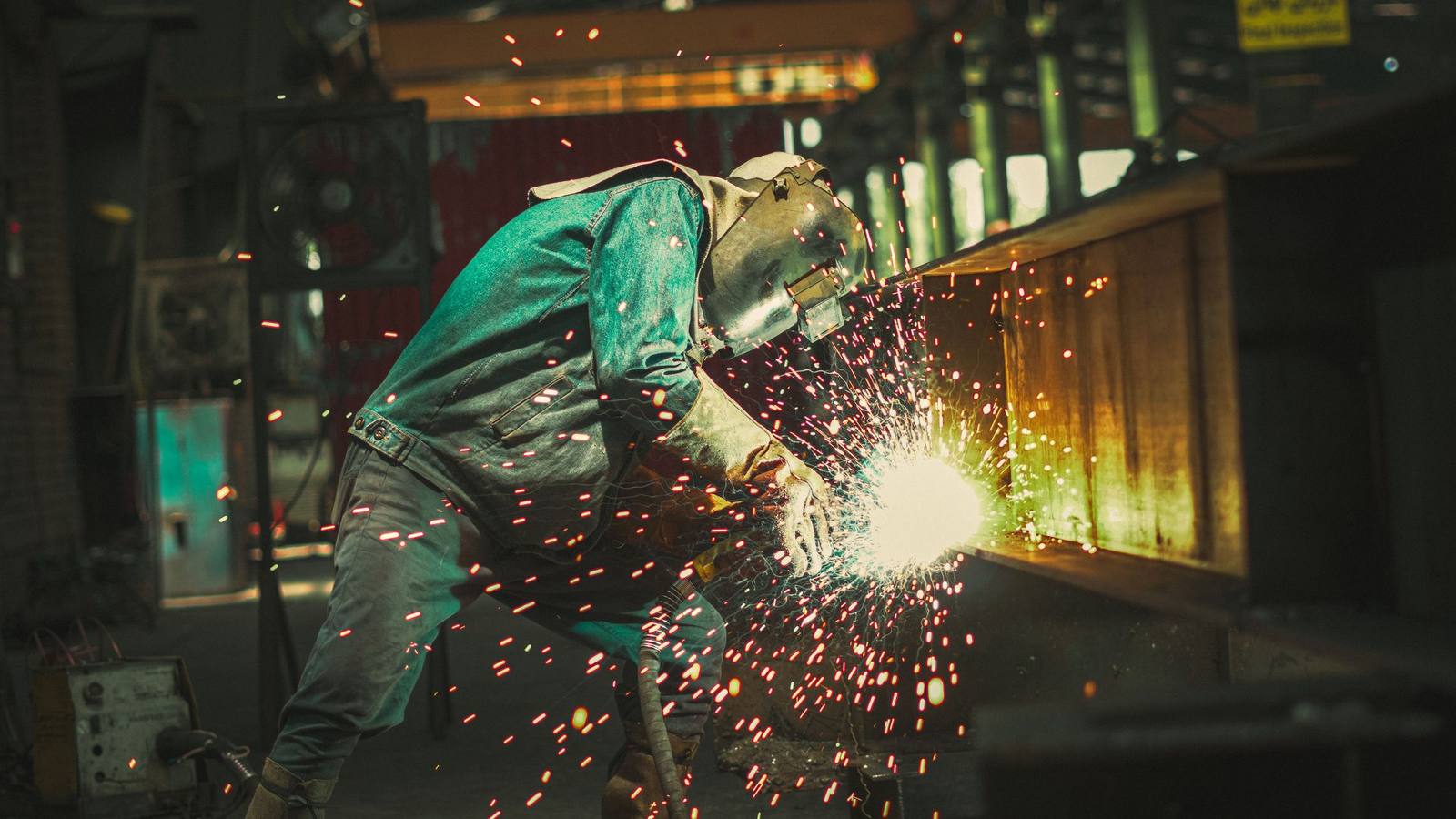 Welder in a helmet welding steel in a workshop with sparks flying, illustrating pipe and steel fabrication