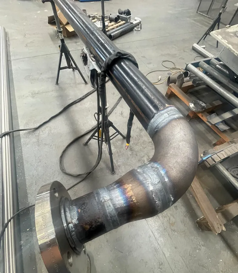 Steel pipe spool with a welded elbow and flange on pipe stands in a workshop