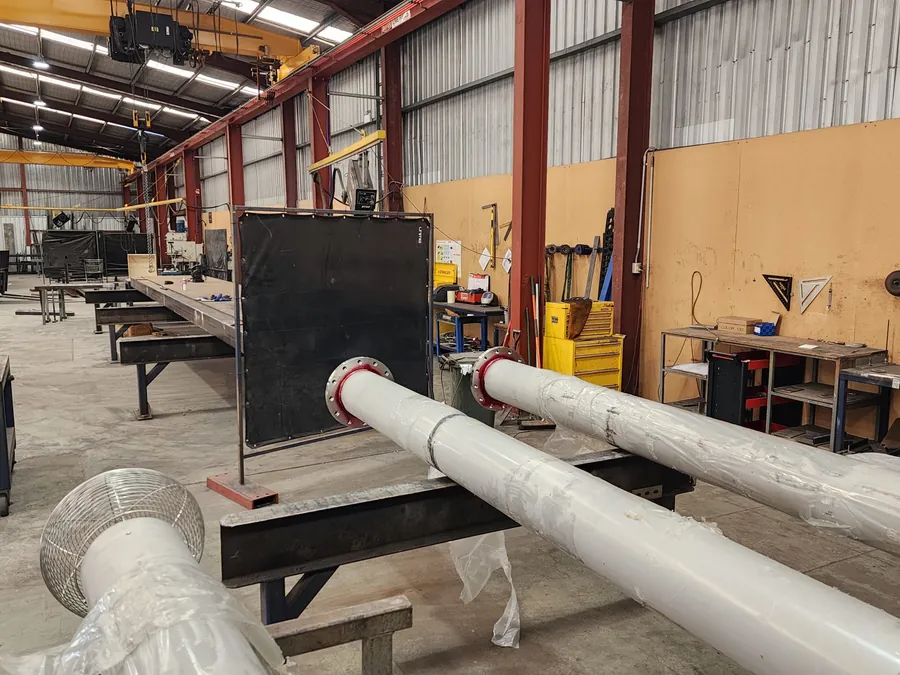 Wrapped vent shaft sections with flanged ends and a wire cowl on stands in a fabrication workshop