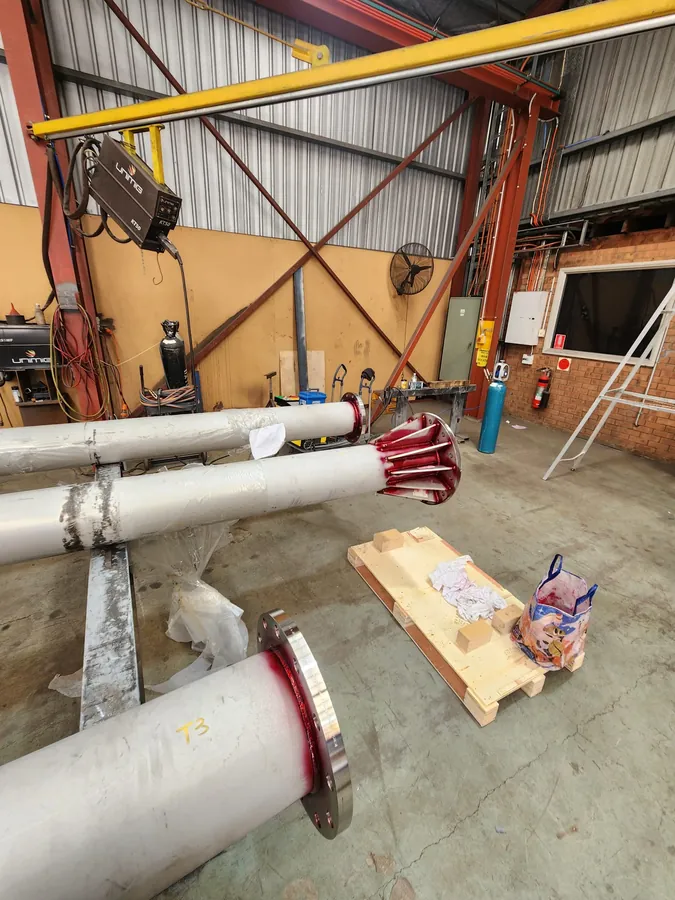 Vent shaft sections with flanged ends on supports in a fabrication workshop